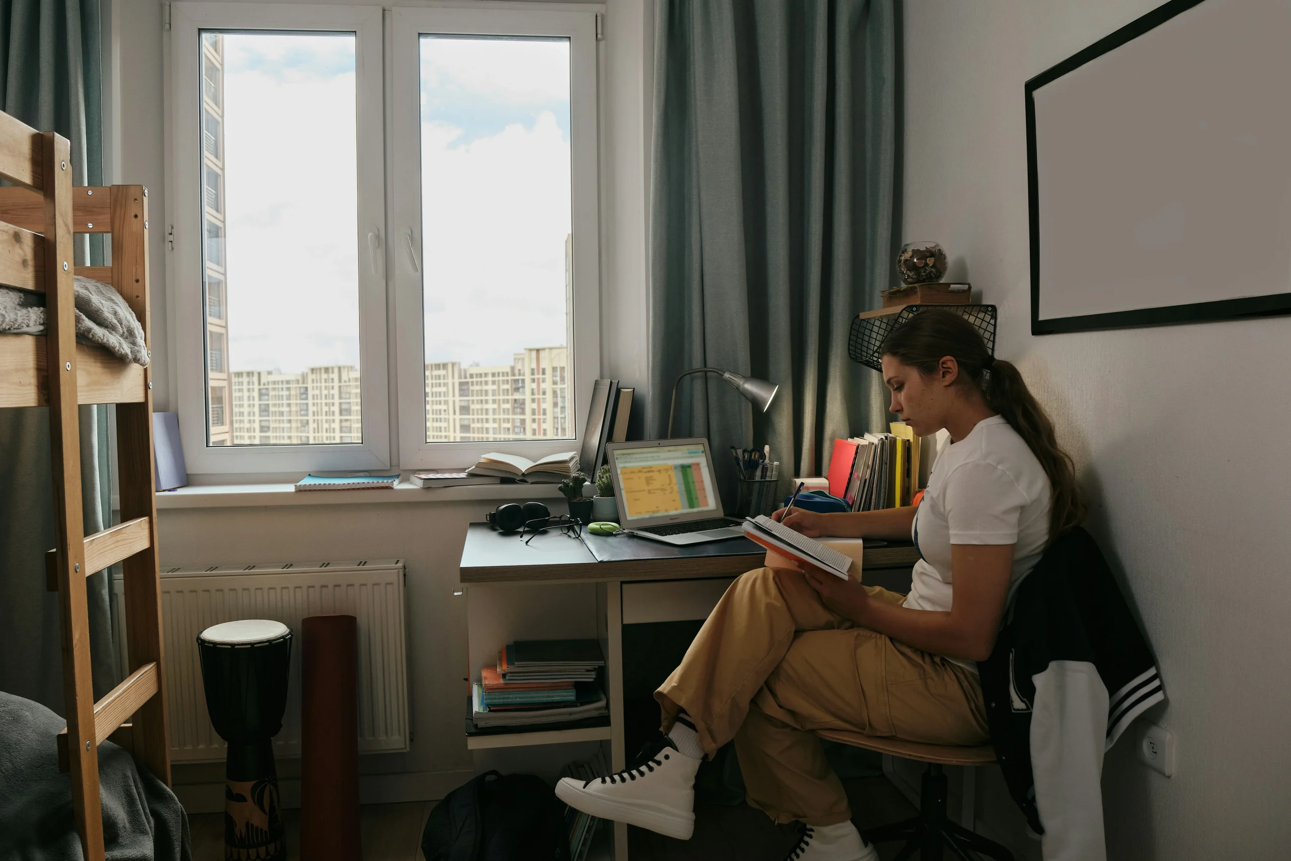 A young woman sitting on a bunk bed reading a book inside a cosy room, showing a comfortable student accommodation in the UK.
